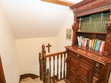 A wooden staircase with a carved wooden bookshelf filled with books and a crucifix on the wall at The Old Chapel in Foxley near Bawdeswell