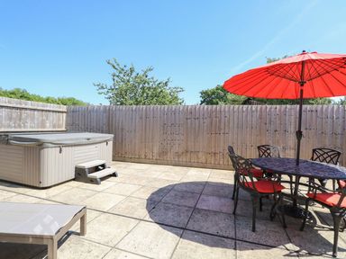 An outdoor patio with a hot tub a table with chairs and a red umbrella at The Old Chapel in Foxley near Bawdeswell