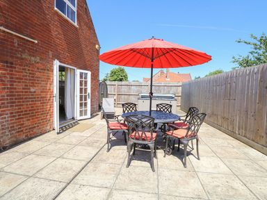A patio area with a round table and six chairs under a red umbrella next to a brick house at The Old Chapel in Foxley near Bawdeswell