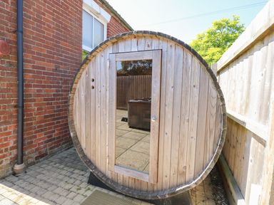 A wooden barrel sauna outside next to a brick wall and wooden fence at The Old Chapel in Foxley near Bawdeswell