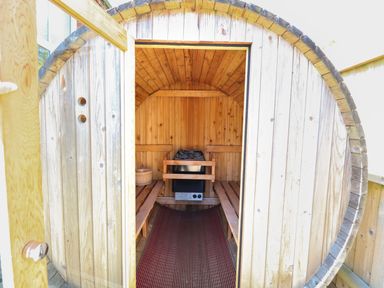 The interior of a small wooden barrel sauna with benches on each side and a heater in the center at The Old Chapel in Foxley near Bawdeswell