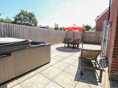 An outdoor patio with a hot tub a table with chairs and a red umbrella and a lounge chair at The Old Chapel Foxley near Bawdeswell