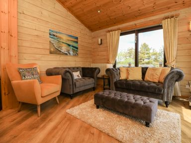 A living room with two grey sofas a beige armchair a long grey ottoman and a large window at Moonlake Lodge in Woolsery near Woolfardisworthy