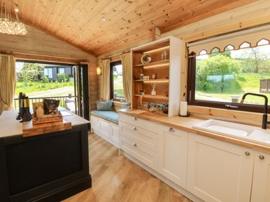 A kitchen with white cabinets wooden countertops a sink window seating area and open patio doors at Moonlake Lodge in Woolsery near Woolfardisworthy
