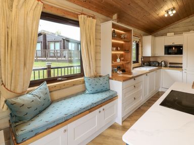 A kitchen with white cabinets a built in microwave a sink an induction hob and a window seat with blue cushions at Moonlake Lodge in Woolsery near Woolfardisworthy