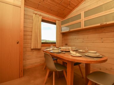 A dining area with a wooden table set for four with dishes and glasses and chairs near a window with curtains at Moonlake Lodge in Woolsery near Woolfardisworthy