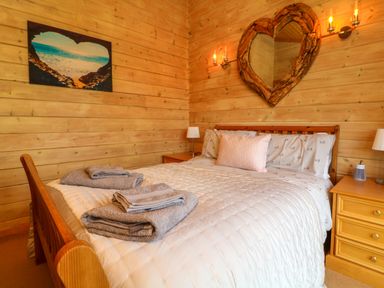 A bedroom with a wooden bed a heart shaped mirror on the wall and folded towels on the bed at Moonlake Lodge in Woolsery near Woolfardisworthy