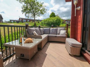 An outdoor seating area with a wicker sofa set a glass coffee table with bread and drinks and a cushioned bench at Moonlake Lodge in Woolsery near Woolfardisworthy