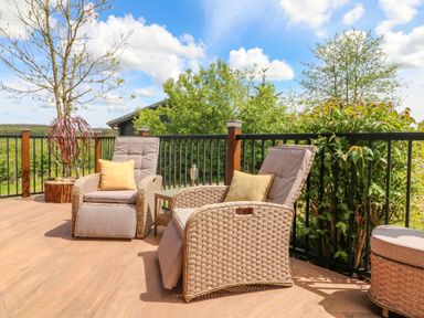 An outdoor patio with two cushioned wicker chairs a small table and plants near a railing at Moonlake Lodge in Woolsery near Woolfardisworthy
