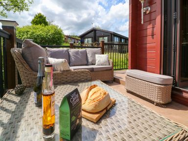 An outdoor patio with wicker furniture a loaf of bread and bottles on a glass table at Moonlake Lodge in Woolsery near Woolfardisworthy