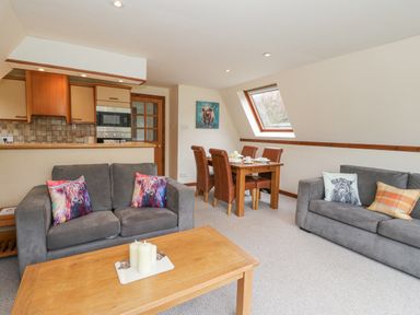 A living room with two grey sofas, a wooden coffee table with white candles, a dining table with four brown chairs, and a kitchen area at Lodge 2 - Inglewood Lodge in Spean Bridge