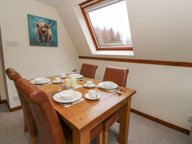 A dining area with a wooden table and four brown chairs set with white dishes and candles under a slanted window at Lodge 2 - Inglewood Lodge in Spean Bridge