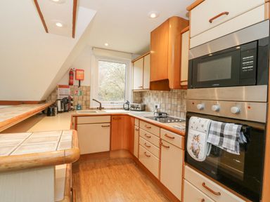 A kitchen with wooden cabinets a microwave oven an oven a sink and a window at Lodge 2 - Inglewood Lodge in Spean Bridge