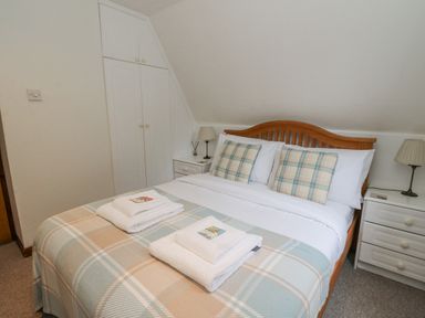 A bedroom with a double bed with plaid pillows and matching blanket two bedside tables with lamps and a built in wardrobe at Lodge 2 - Inglewood Lodge in Spean Bridge