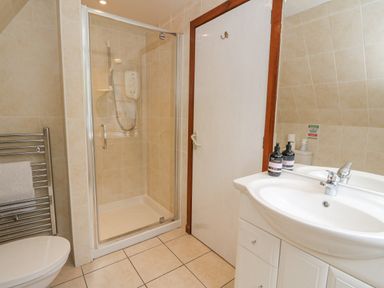 A bathroom with a shower cubicle, sink with a mirror, towel rail, and a door at Lodge 2 - Inglewood Lodge in Spean Bridge