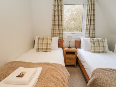 A bedroom with two single beds a wooden nightstand a lamp and a window at Lodge 2 - Inglewood Lodge in Spean Bridge