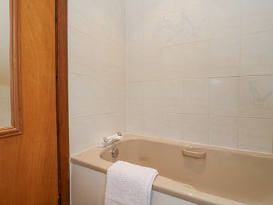 A bathroom with a beige bathtub a white towel on the edge and white tiled walls with bird designs at Lodge 2 - Inglewood Lodge in Spean Bridge