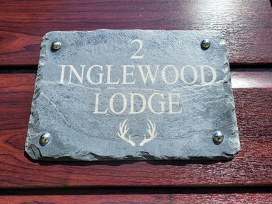 A stone sign with the text 2 Inglewood Lodge and antlers mounted on a wooden surface at Lodge 2 - Inglewood Lodge in Spean Bridge