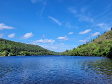 A lake surrounded by green hills and trees under a blue sky at Lodge 2 - Inglewood Lodge in Spean Bridge