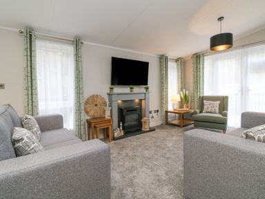 A living room with two gray sofas a green armchair a fireplace and a wall mounted tv at 18 Manleigh Park in Combe Martin