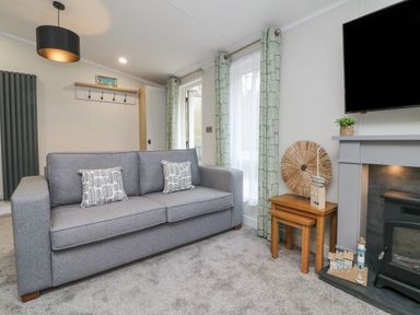 A living room with a grey sofa two patterned cushions wooden nesting tables a fireplace and a mounted television at 18 Manleigh Park in Combe Martin