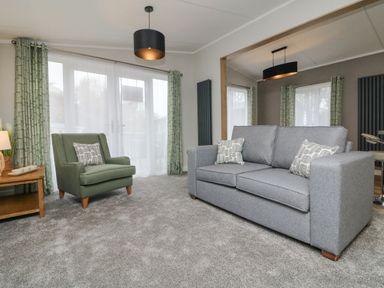 A living room with a gray sofa and green armchair near windows with green curtains at 18 Manleigh Park in Combe Martin