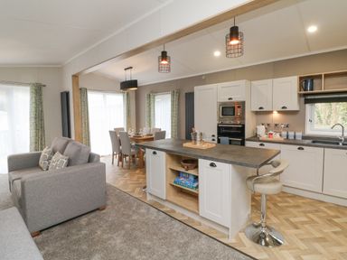 An open plan kitchen and dining area with a grey sofa and bar stool at 18 Manleigh Park in Combe Martin