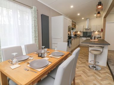 A kitchen and dining area with a wooden table set for four and a kitchen island with a bar stool at 18 Manleigh Park in Combe Martin