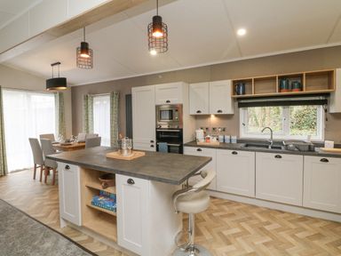 A kitchen with a central island and dining table next to windows at 18 Manleigh Park in Combe Martin