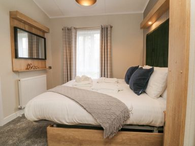 A bedroom with a bed with pillows and towels and a wall-mounted mirror at 18 Manleigh Park in Combe Martin