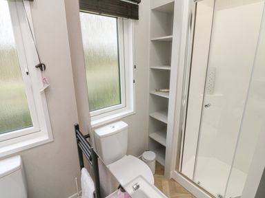 A bathroom with a toilet shower cubicle window and shelves at 18 Manleigh Park in Combe Martin