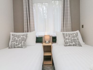 A bedroom with two single beds with patterned pillows and a lamp on a wooden nightstand between them at 18 Manleigh Park in Combe Martin