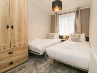 A bedroom with two single beds bedside table lamp and wooden wardrobe at 18 Manleigh Park in Combe Martin