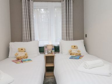 A bedroom with two single beds with teddy bears and books separated by a small wooden nightstand at 18 Manleigh Park in Combe Martin