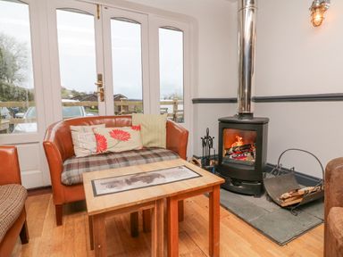 A sitting area with a wood burning stove a wooden coffee table and a sofa with cushions at 18 Manleigh Park in Combe Martin