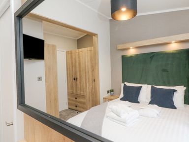 A bedroom with a bed with pillows and towels next to a wooden wardrobe and a wall-mounted television at 18 Manleigh Park in Combe Martin