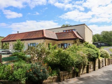 A building with a tiled roof surrounded by plants and a wooden fence at 18 Manleigh Park in Combe Martin