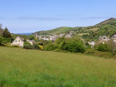A grassy field with houses and hills in the background at 18 Manleigh Park in Combe Martin