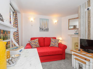 A living room with a red sofa and patterned cushions next to a white table with a television on it at Sea Pinks in Looe