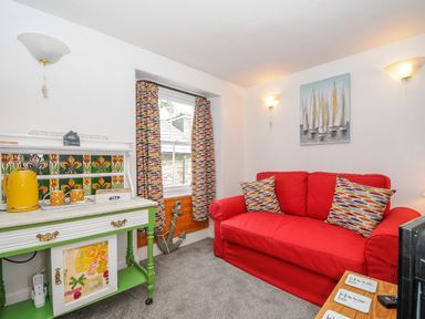 A room with a red sofa cushions curtain and a table with a yellow kettle and cups at Sea Pinks in Looe