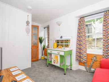A room with a green sideboard white walls carpet and colorful fish patterned curtains at Sea Pinks in Looe