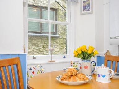 A kitchen table with croissants flowers and a teapot near a window at Sea Pinks in Looe