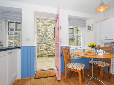 A kitchen dining area with wooden chairs and a round table next to an open pink door at Sea Pinks in Looe