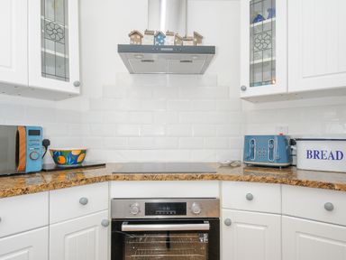 A kitchen countertop with a microwave toaster bread bin and oven at Sea Pinks in Looe
