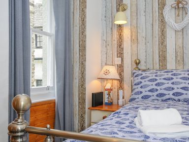 A bedroom with a metal bed frame blue patterned bedding and a bedside table with a lamp at Sea Pinks in Looe