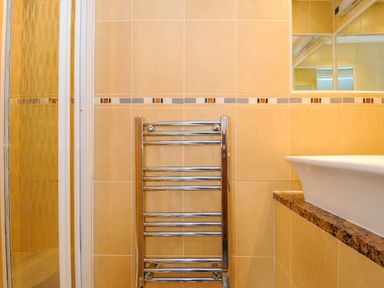 A bathroom with a chrome towel radiator a white basin with a granite countertop and a shower cubicle at Sea Pinks in Looe