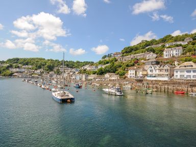 A harbor with boats moored in the water by houses on a hillside at Sea Pinks in Looe