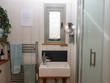A bathroom with a sink a window a towel rack with towels a shower cubicle and a mirror at Burr 2 Shepherds Hut Swimbridge near Barnstaple