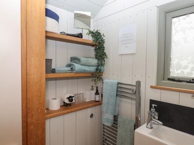 A bathroom corner with wooden shelves holding towels and toiletries a towel rack with towels a small window and a sink at Burr 2 Shepherds Hut Swimbridge near Barnstaple