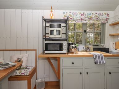 A kitchen corner with a microwave and air fryer on a metal rack and a wooden countertop with a sink near a window at Burr 2 Shepherds Hut Swimbridge near Barnstaple